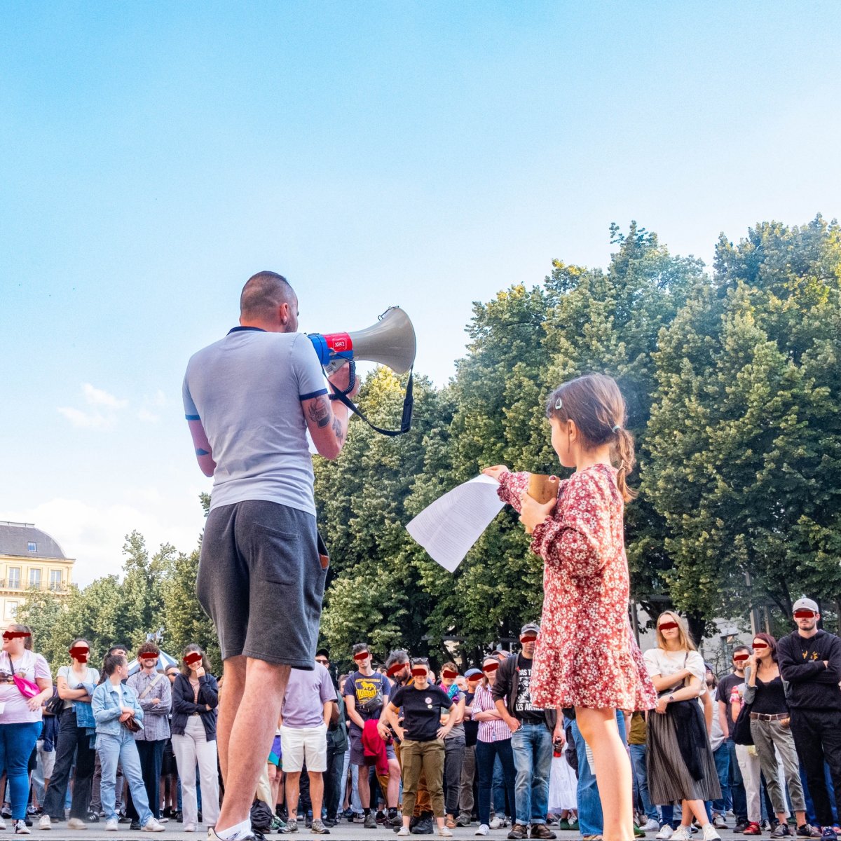 Une enfant fait passer les notes du discours à un orateur au mégaphone fasse à une foule